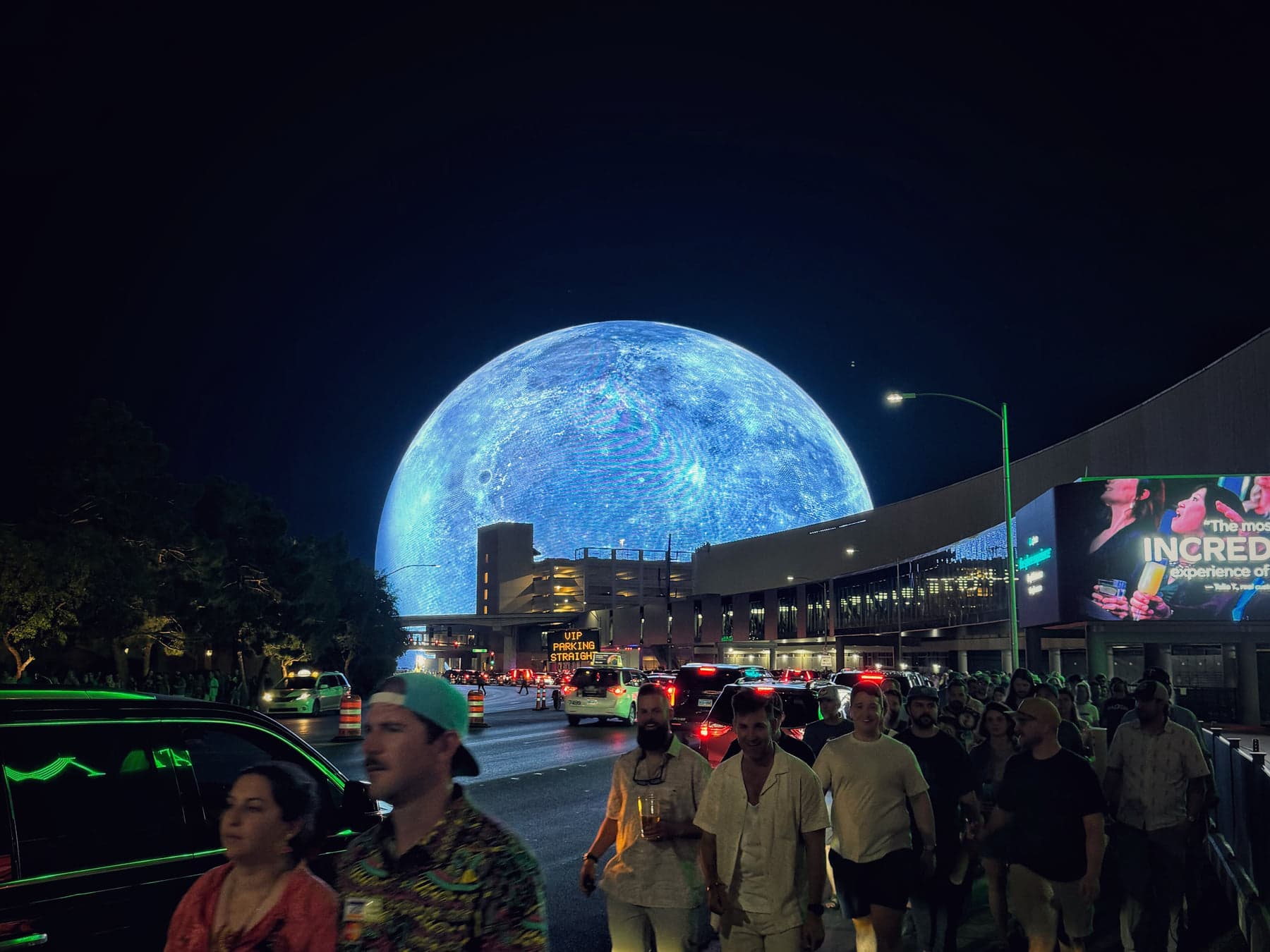 The Sphere lit as a moon above a crowd on the street.